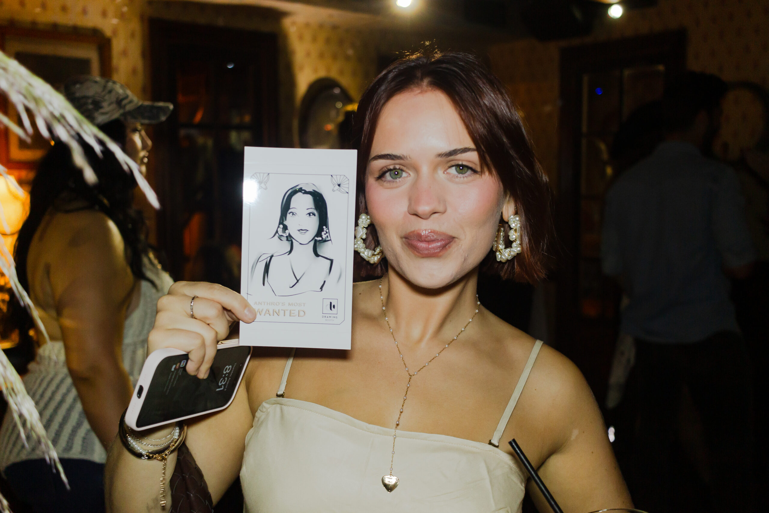 A guest at Anthropologie's Anthro Saloon event in NYC holds up their custom "Wanted Poster" sketch created by Drawing Booth, showcasing their portrait in a Western-themed design.