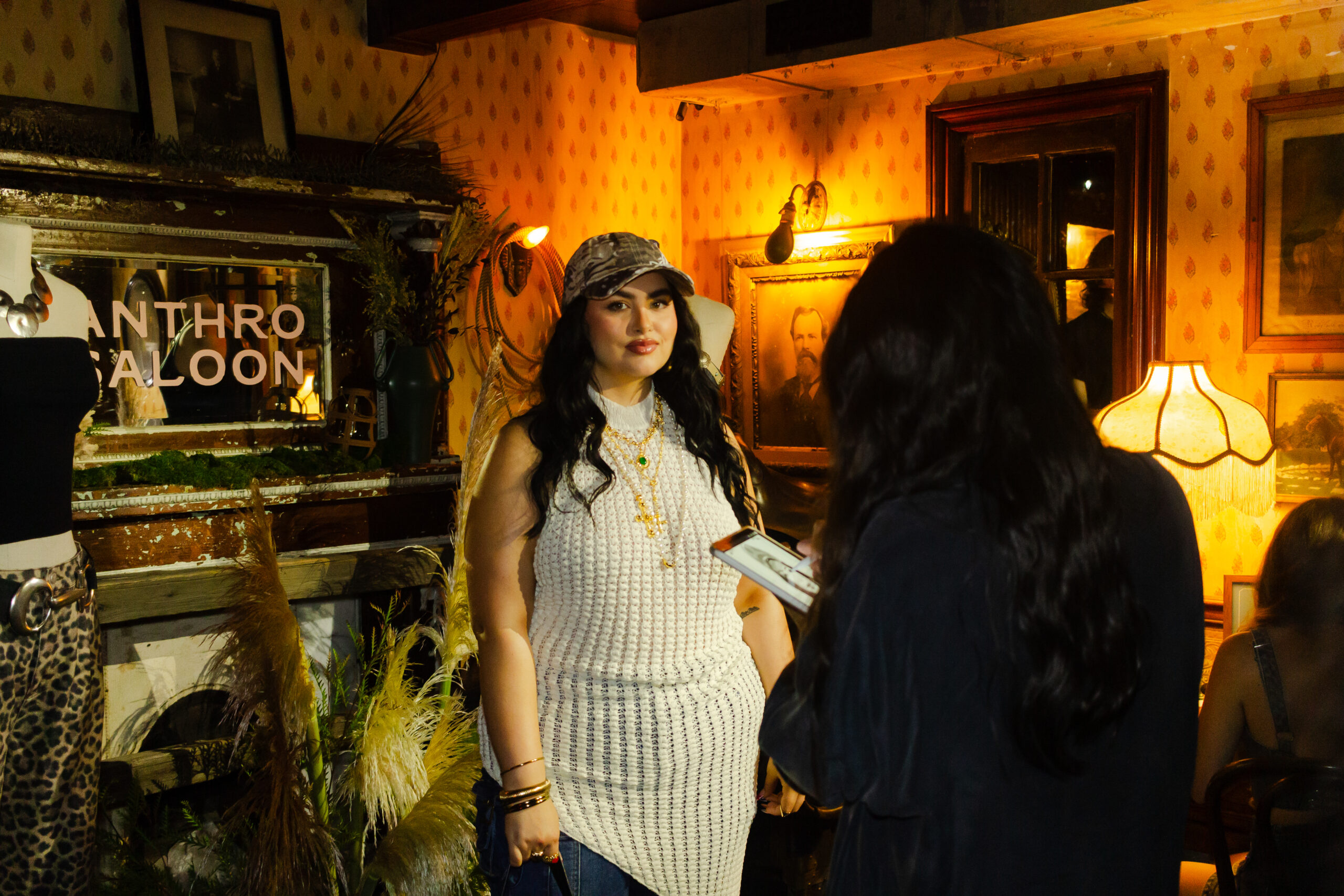 A guest at Anthropologie's Anthro Saloon event in NYC holds up their custom "Wanted Poster" sketch created by Drawing Booth, showcasing their portrait in a Western-themed design.